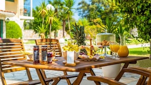 Mesa al aire libre con diversos alimentos y bebidas, rodeada de sillas de madera.