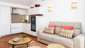 Une cuisine moderne avec des meubles blancs, un canapé gris agrémenté de coussins colorés et une petite table ronde sur laquelle est posée une plante.