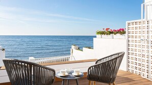Un balcon avec deux fauteuils en osier, une petite table avec des tasses et une vue sur la mer.