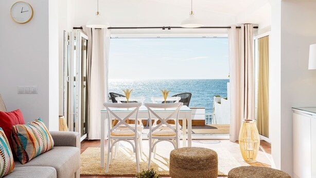 Une pièce avec vue sur la mer, une table à manger avec des chaises, un canapé et un grand vase.