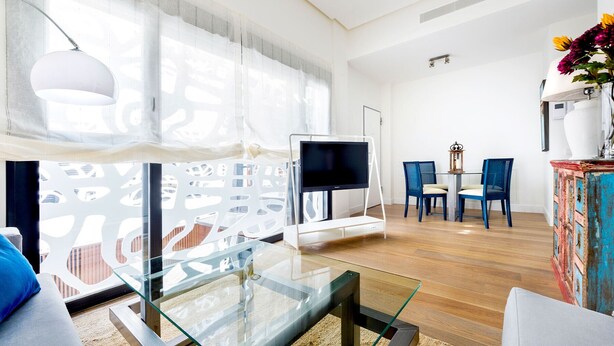 A modern living room with a glass coffee table, a sofa, a TV on a stand, and a dining area with chairs. - Genteel Home Mateos Gago II (Seville)