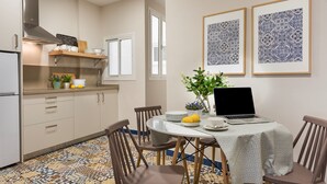 A compact kitchen with a dining area, featuring a laptop on the table, a refrigerator, and a window.