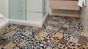 A modern bathroom with a glass-enclosed shower, a white tiled floor, and a wooden vanity with a mirror above it.