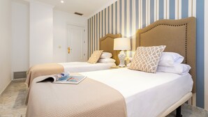 A hotel room with two beds, striped wallpaper, and a magazine on the bed. - Genteel Home Isabel Católica I (Granada)