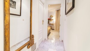 A hallway with a marble floor, a wooden-framed mirror, and a bed with a lamp and flowers in the background. - Genteel Home Isabel Católica I (Granada)