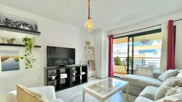 A modern living room with a flat-screen TV, white sofas, a glass coffee table, and a balcony with a view of buildings. - Ricardo Soriano   EaW Homes (Marbella)