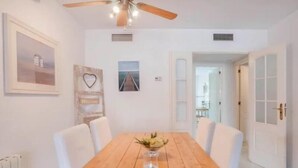 A dining room with a wooden table, white chairs, a ceiling fan, and a wall-mounted picture frame. - Ricardo Soriano   EaW Homes (Marbella)