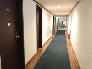 Stroll through the well-lit corridor with doors leading to comfortable rooms.