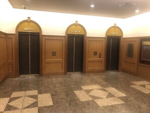 Een hal met vier houten liftdeuren, een patroon vloer en een beveiligingscamera aan het plafond.