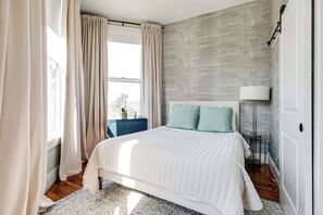 A bedroom with a bed, a nightstand, a lamp, and a window with curtains.