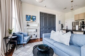 A modern living room with a blue sofa, a coffee table, and a bookshelf. - Newly Renovated, Spacious Suite with Every Luxury (Richmond)