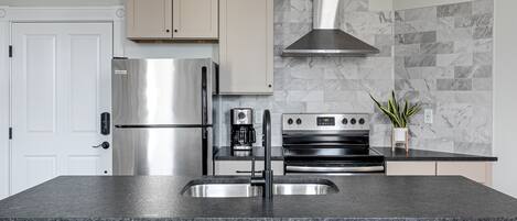Una cocina moderna con un refrigerador de acero inoxidable, un horno empotrado y una encimera negra.
