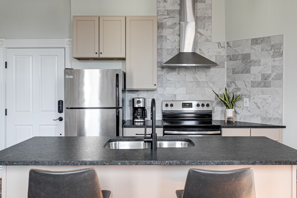 A modern kitchen with a stainless steel refrigerator, a built-in oven, and a black countertop. - Newly Renovated, Spacious Suite with Every Luxury (Richmond)