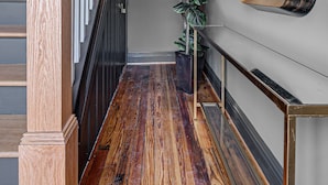 Un pasillo con una escalera de madera, una planta en maceta y un espejo colgado en la pared.