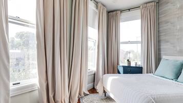A bedroom with a large bed, a nightstand, and a window with curtains.