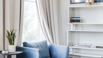 A modern living room with a blue sofa, a white bookshelf, and a potted plant.