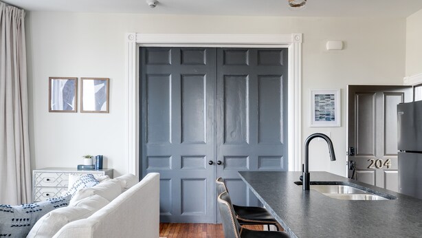 Cocina moderna con encimera oscura, un lavamanos y un refrigerador. Cuenta con una zona de comedor con un banco y sillas.