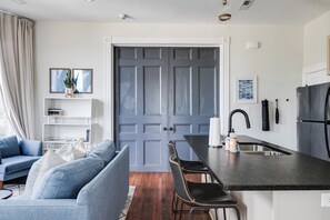 A modern kitchen with a grey door, a dining area with a bar, and a living room with a blue sofa.