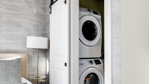 A hotel room with a bed, a lamp, and a stacked washer and dryer.