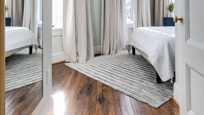 Un dormitorio con piso de madera, dos camas, un espejo grande y cortinas color crema.
