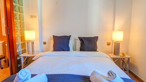 Habitació d'hotel amb un llit, dues làmpades de nit, una taula petita i una paret amb un panell decoratiu.