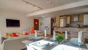 Un saló modern amb zona de menjador preparada per a quatre, cuina amb salabost i televisió plana penjada a la paret.
