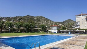 Una piscina d'aigua cristal·lina i blava, envoltada d'un solàrium enrajolat, amb una muntanya al fons.