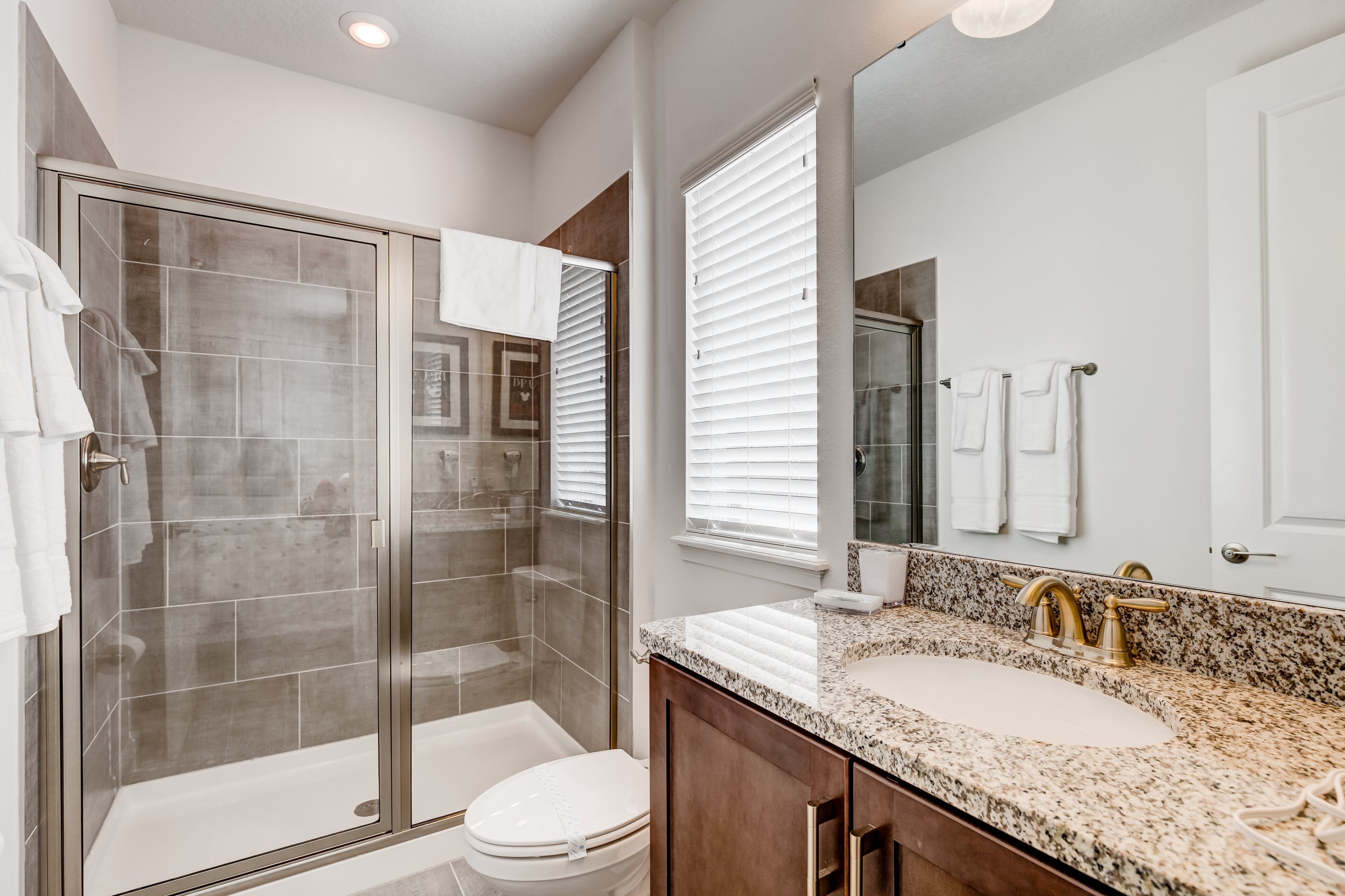 A modern bathroom with a glass-enclosed shower, a white toilet, a granite countertop sink, and a large mirror.