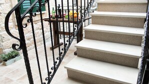 Eine Treppe mit beigem Teppichboden und schwarzen schmiedeeisernen Geländern, die zu einem Balkon mit einem Blumentopf und einem Tisch mit Flaschen und Früchten führt.