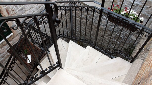 Eine Marmortreppe mit schwarzen schmiedeeisernen Geländern und einem Blumentopf auf der Podestfläche.