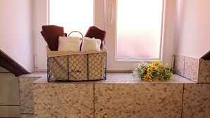 Ein Badezimmer mit Wand aus Mosaikfliesen, einem Fenster mit satiniertem Glas und einem Korb mit Handtüchern und einem Blumenstrauß.