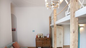 Una stanza con pavimento in parquet a spina di pesce, un divano con cuscini, un armadio in legno e un lampadario.