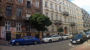 Una strada fiancheggiata da edifici a più piani, auto parcheggiate e un albero.