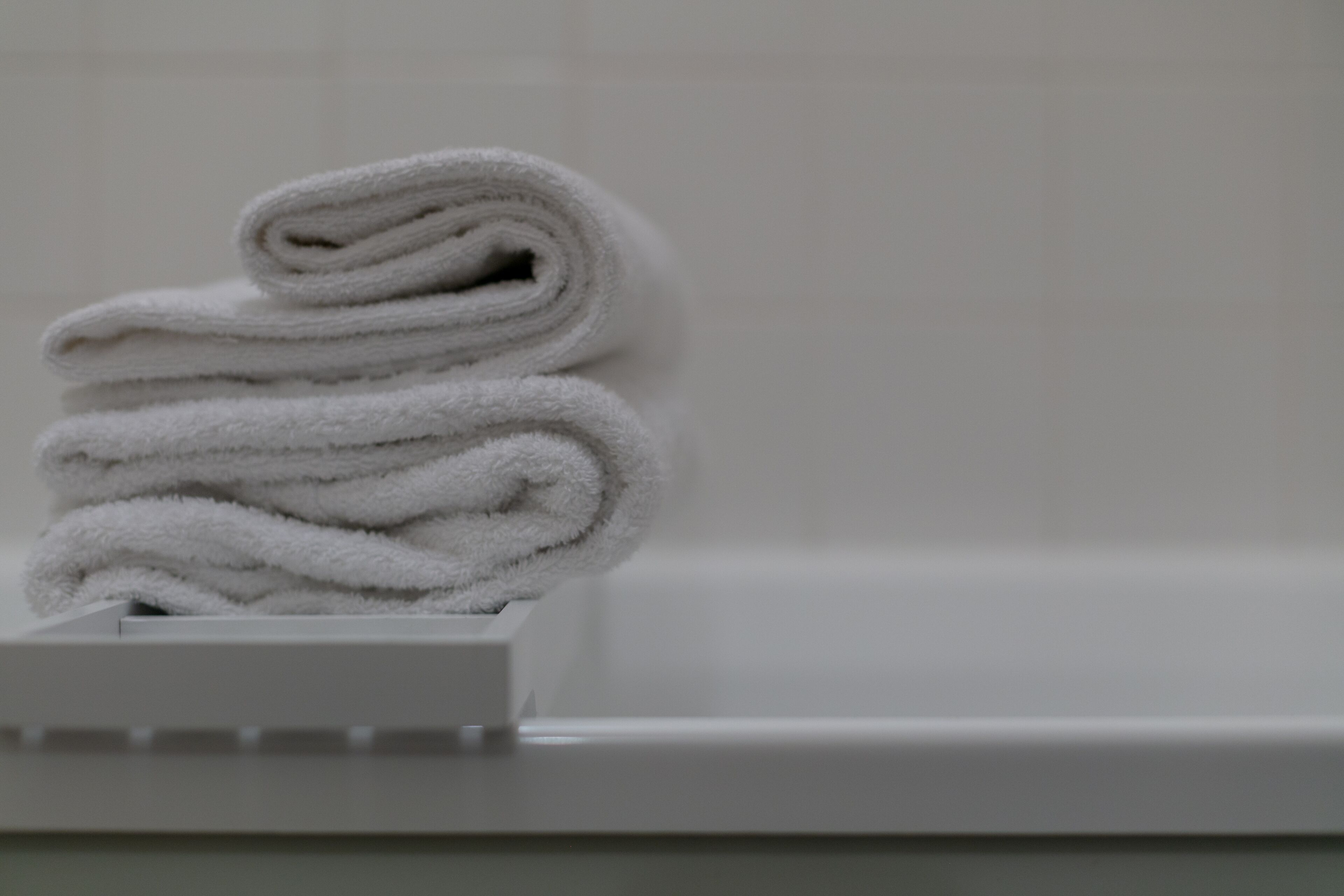 Uma pilha de toalhas brancas sobre um suporte branco em um banheiro.