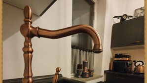 Una cocina con un grifo de cobre, un lavamanos y una tetera sobre la estufa.