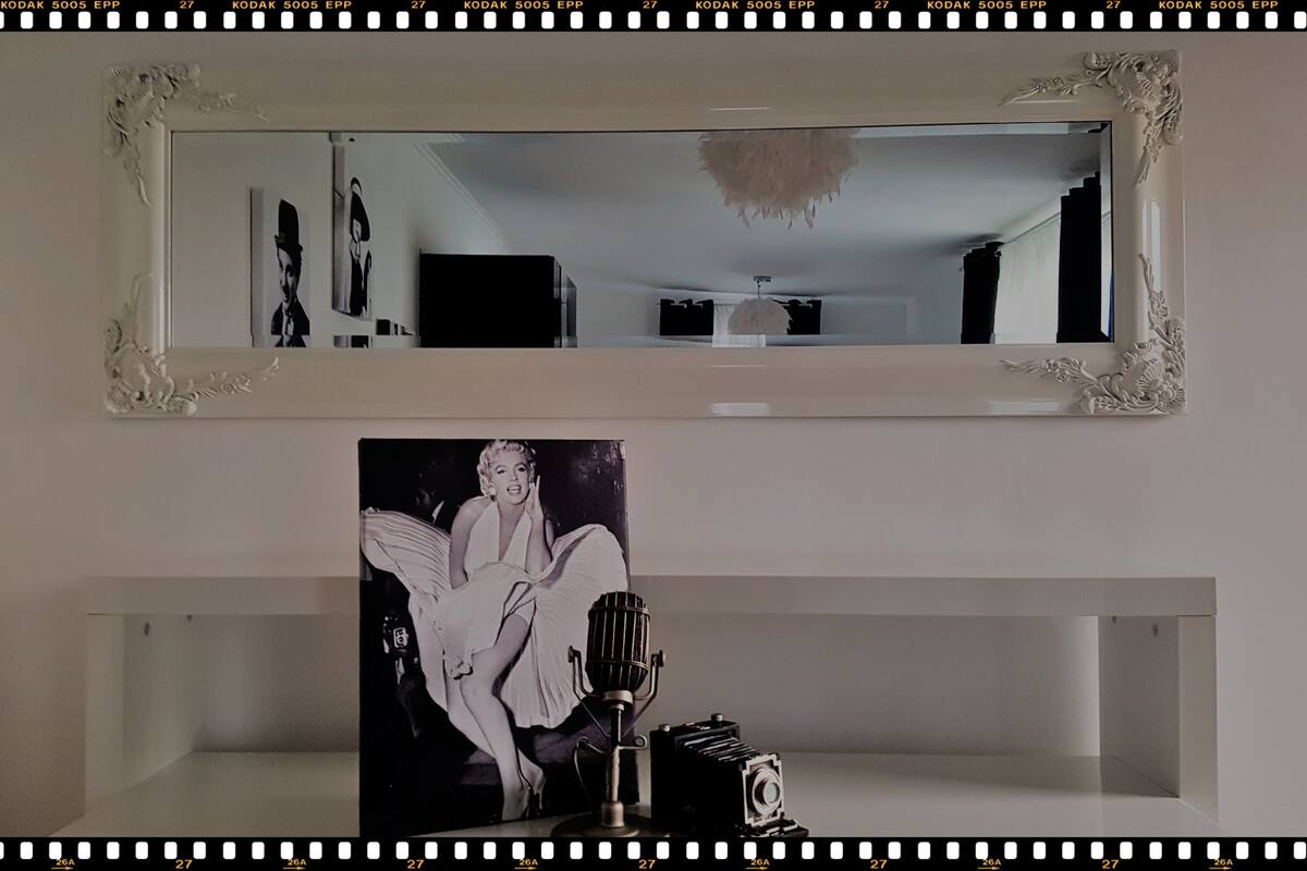 A framed black and white photograph of a woman sitting on a chair, a vintage microphone, and a camera on a white shelf.