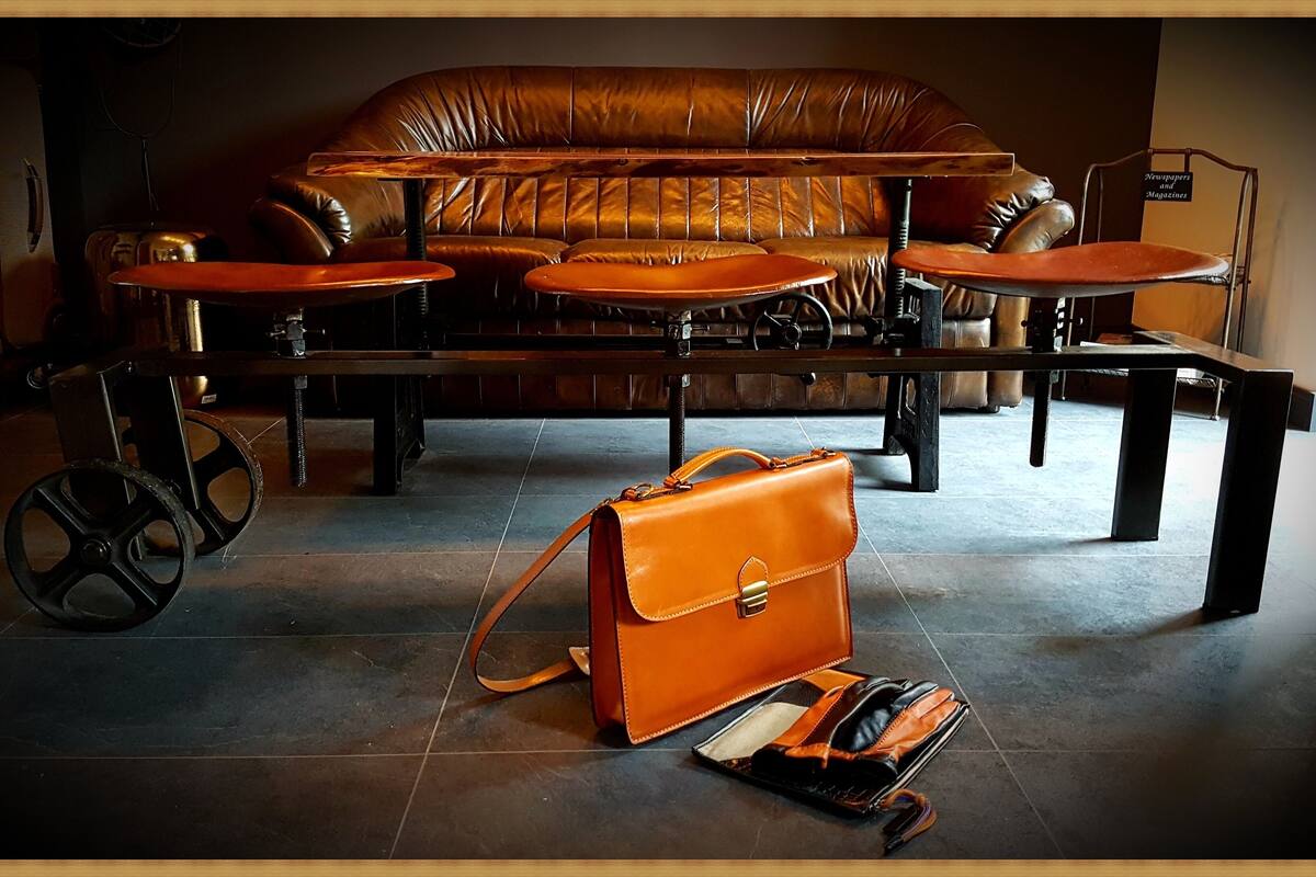 A room with a leather sofa, a wooden coffee table, and a small table with a chair. There is a suitcase and a handbag on the floor.