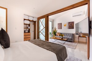 A modern bedroom with a large bed, a wooden wardrobe, a grey sofa, and a TV in the living area. - C A L Suites (Cali)