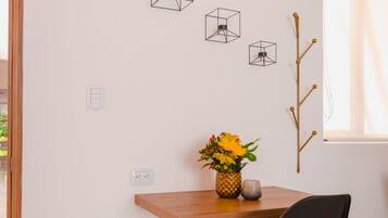 Een moderne kamer met een houten bureau, een zwarte stoel en een vaas met bloemen. Drie geometrische decoraties en een houten tak sieren de wand.