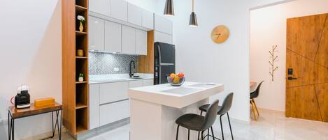 A modern kitchen with a central island, a coffee machine, and a wooden cabinet.