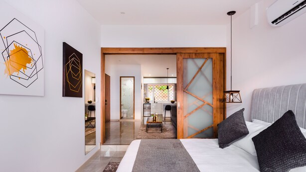A modern bedroom with a large bed, a wooden door, and a view into the living area.