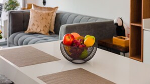 A modern living room with a grey sofa, a white coffee table with a fruit bowl, and two black pendant lights.