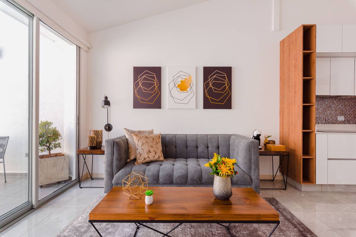 A modern living room with a grey sofa, a wooden coffee table, and three abstract wall art pieces.