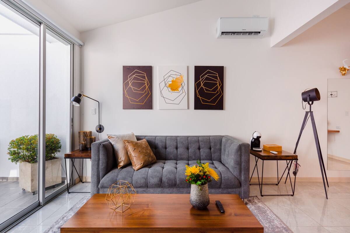 A modern living room with a grey sofa, a wooden coffee table with a vase of flowers, and three abstract paintings on the wall.