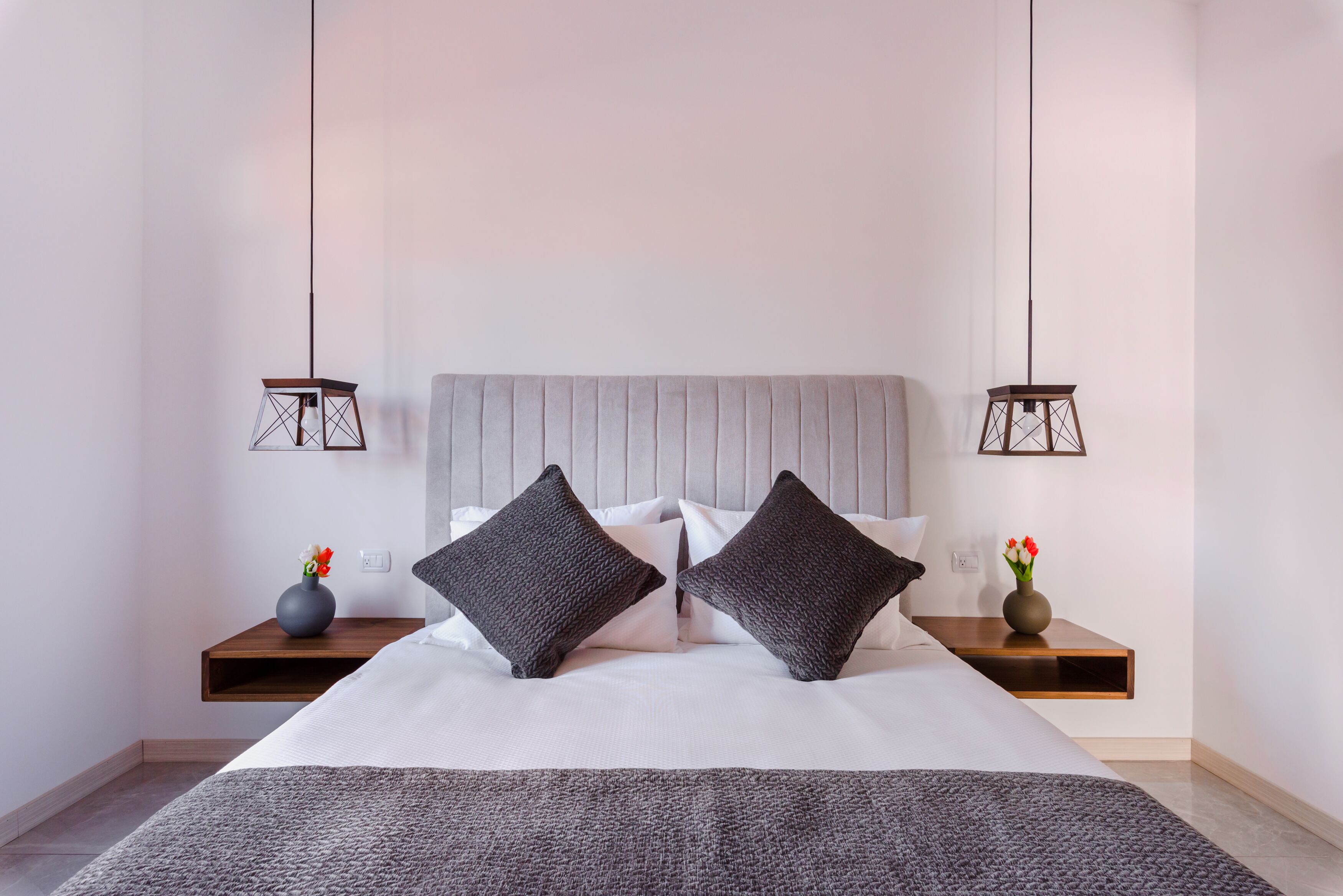 Ein modernes Schlafzimmer mit einem großen Bett, zwei Nachttischen und hängenden Pendelleuchten.