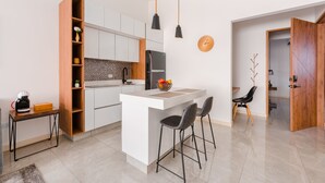 A modern kitchen with white cabinets, a central island, and a small dining area with two chairs.