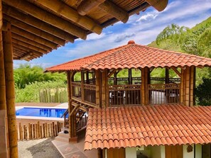 A wooden gazebo with a tiled roof overlooking a swimming pool.
