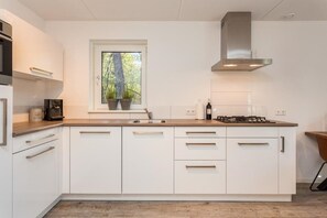 Una cocina moderna con armarios blancos, encimera de madera, una ventana con plantas, una campana extractora de acero inoxidable y un horno empotrado.