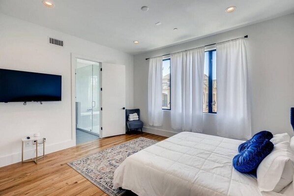 A modern bedroom with a large bed, a flat-screen TV, and a view of the city through the window.