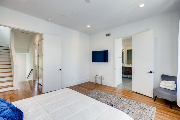 A modern bedroom with a large bed, a flat-screen TV, and a bathroom visible through an open door.
